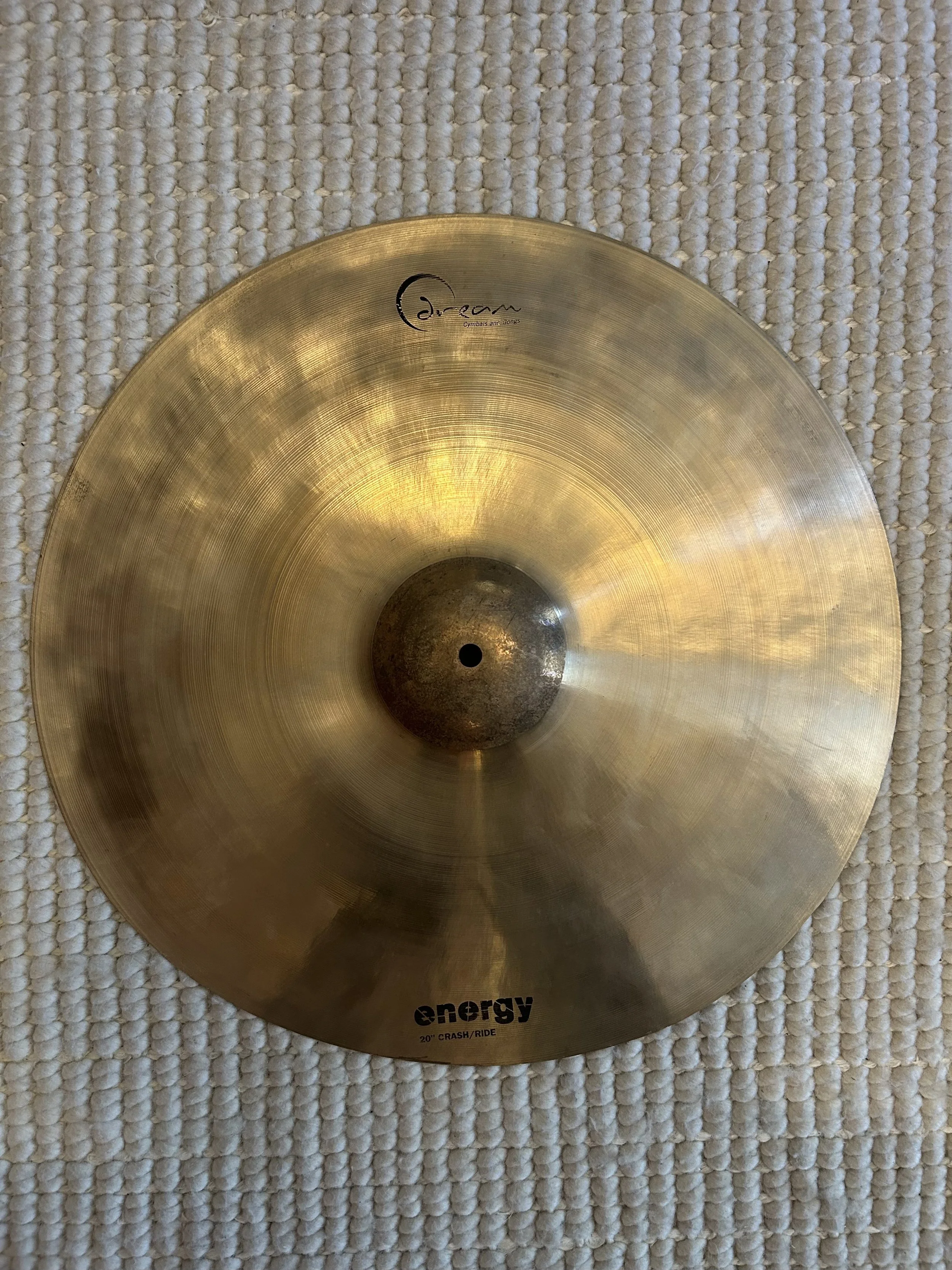 Brass cymbal with the brand name 'Dream' engraved on it, lying on a textured beige surface.