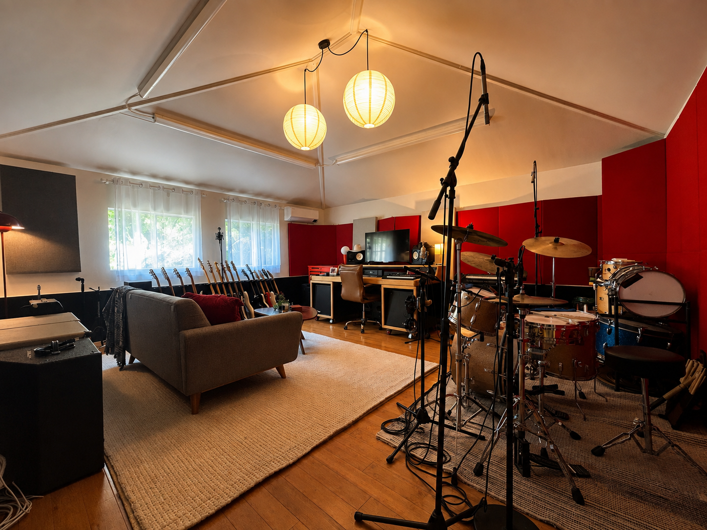 Music studio with guitars, drums, and recording equipment in a cozy room with natural light, red and gray walls, and two hanging paper lanterns.