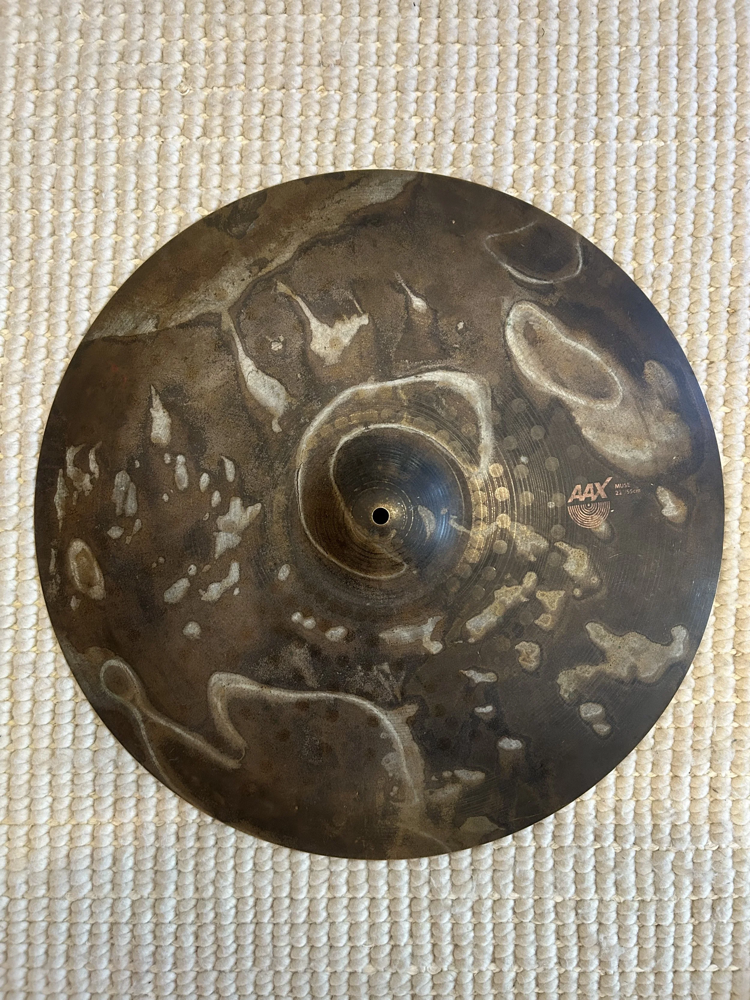 Close-up of a metallic cymbal with a textured surface, resting on a woven beige carpet.