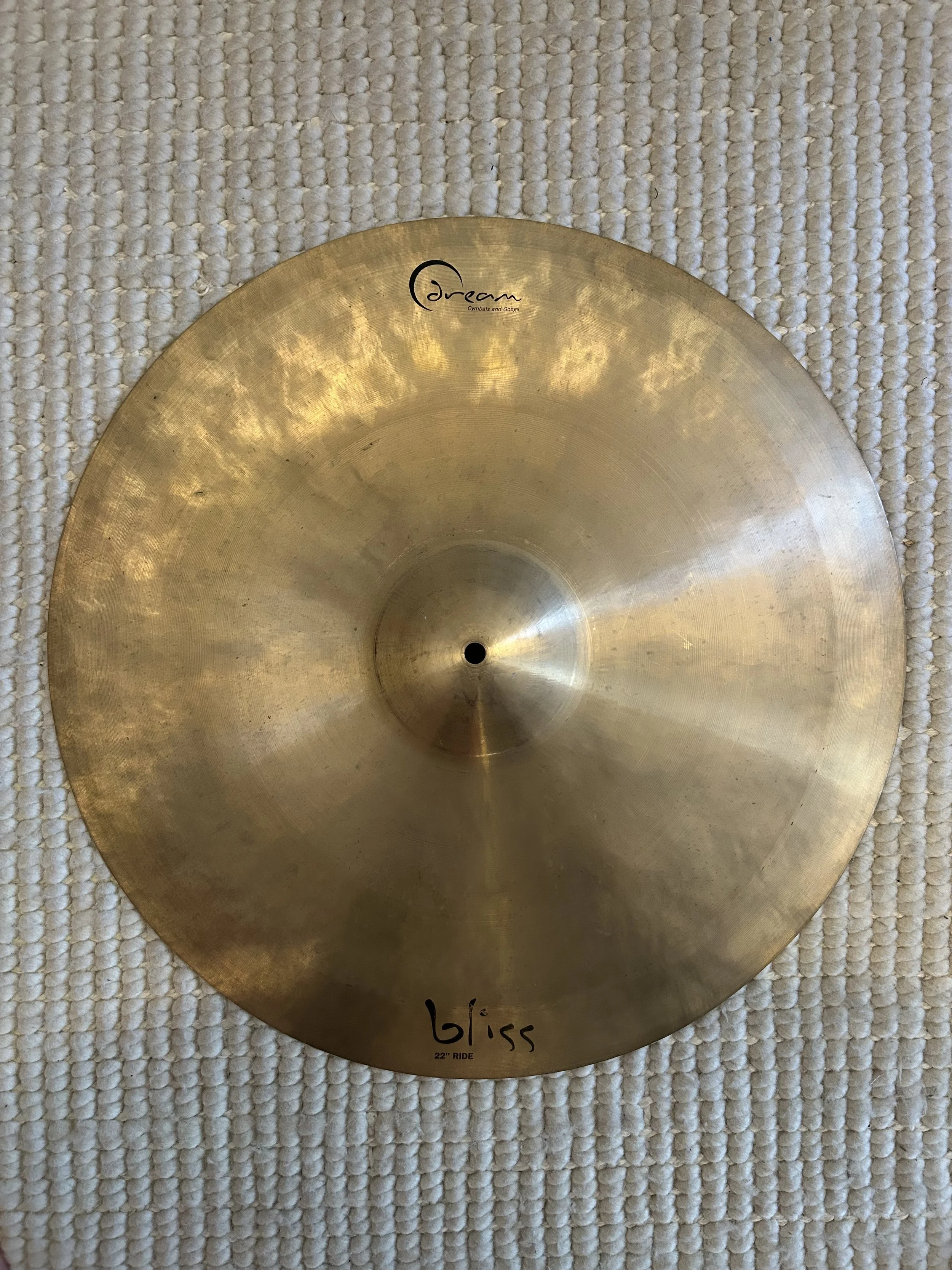 A gold-colored cymbal with the words 'dream cymbals and gong' printed on it, lying on a textured white surface.
