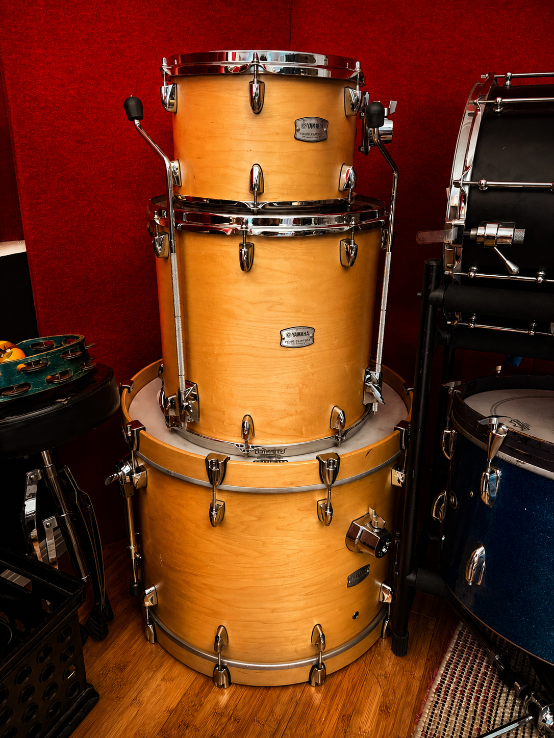 Stacked Yamaha wooden drums in a music studio with red walls and additional percussion instruments nearby.