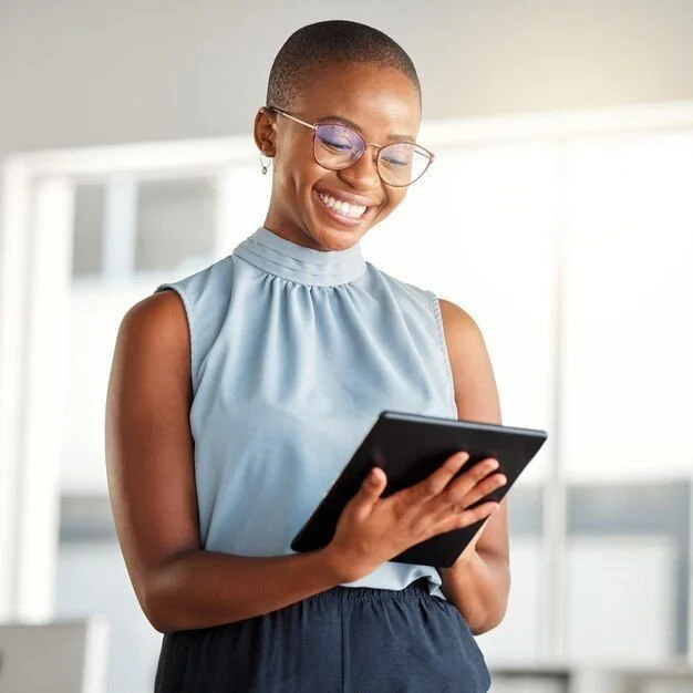 Smiling woman with short hair and glasses using a tablet in a bright room.