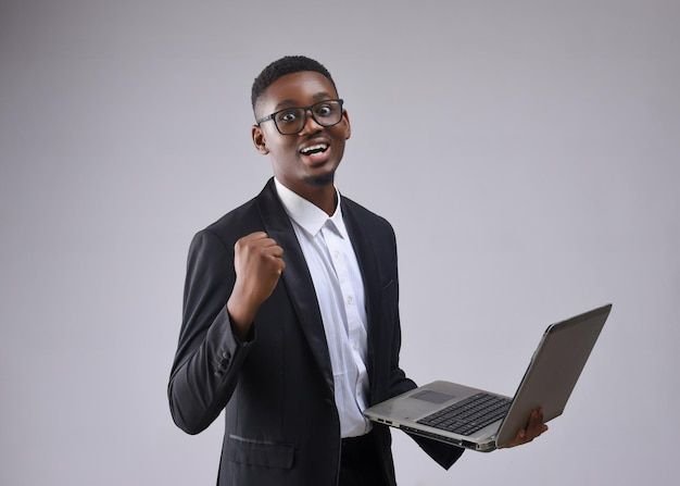 A young man dressed in a business suit holding a laptop and giving a fist pump, smiling confidently.