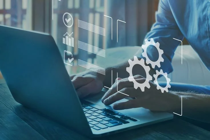 Person working on a laptop with digital icons and gears overlay representing technology and automation.