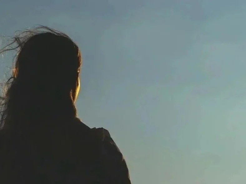 Side view of a woman with long hair looking at the sky during sunset or sunrise.