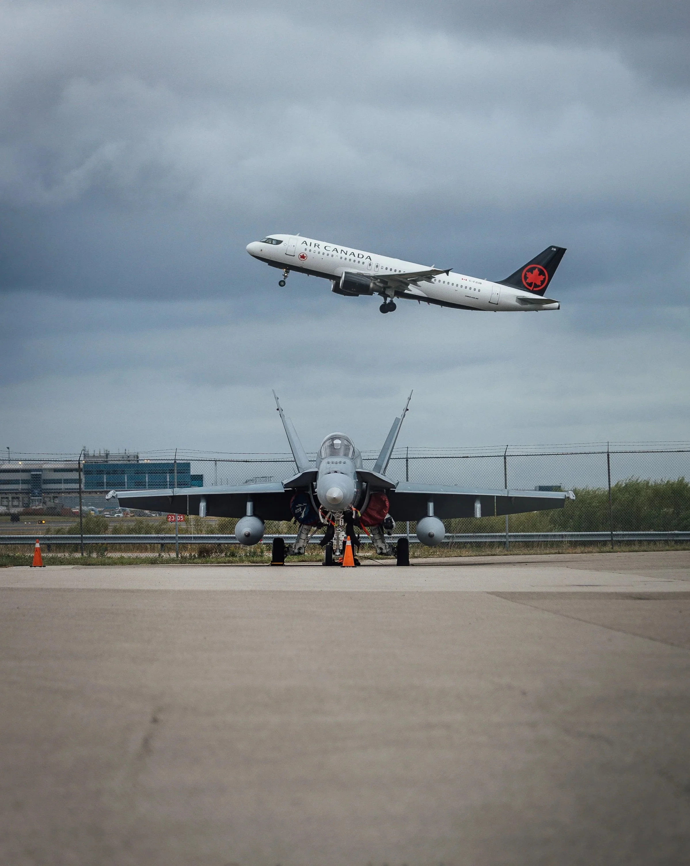 A commercial airplane with 'AIR CANADA' written on the side during takeoff, seen from the front with landing gear still extended, against a cloudy sky.