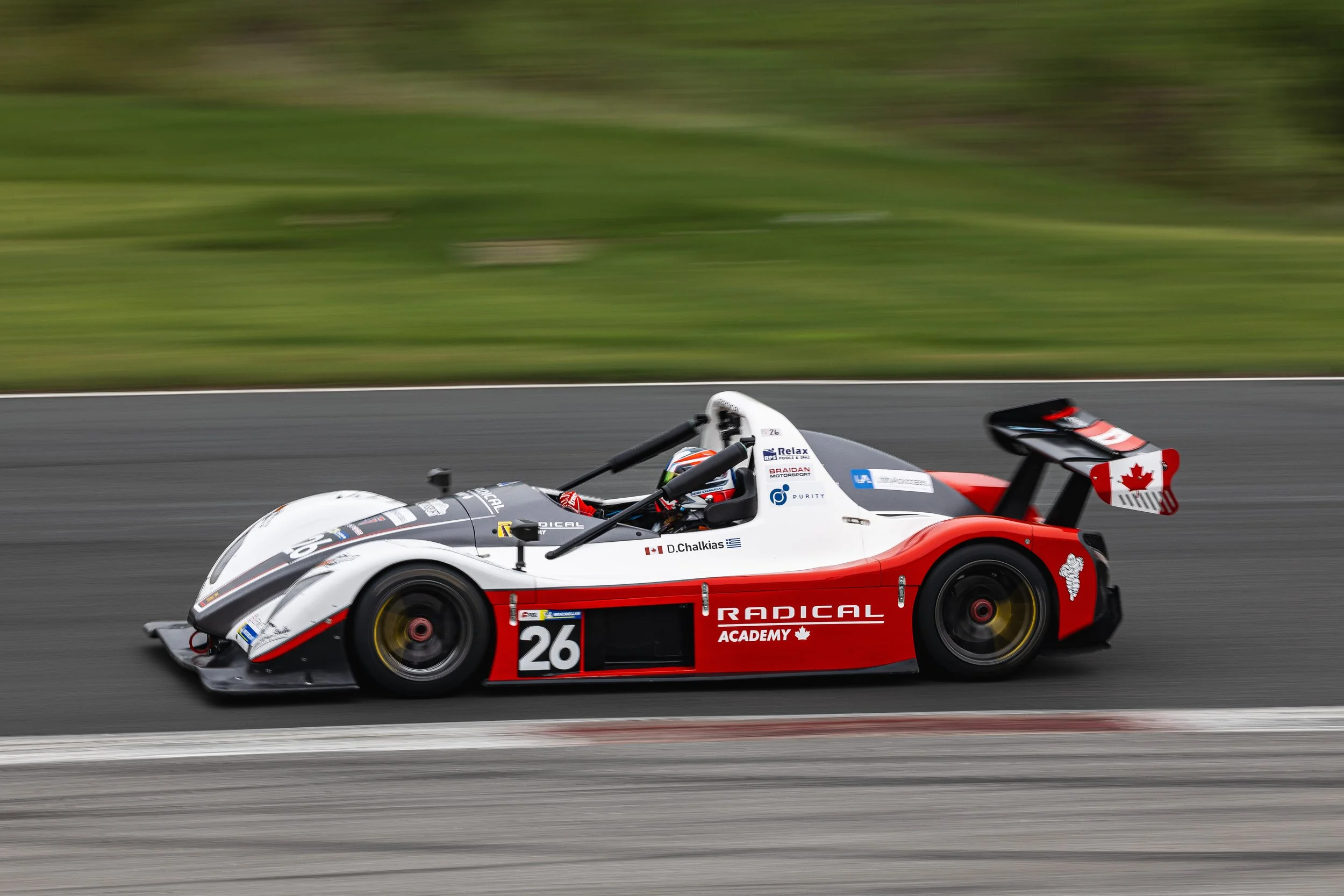 A race car with red, white, and black colors speeding on a racetrack, with a green blurred background.