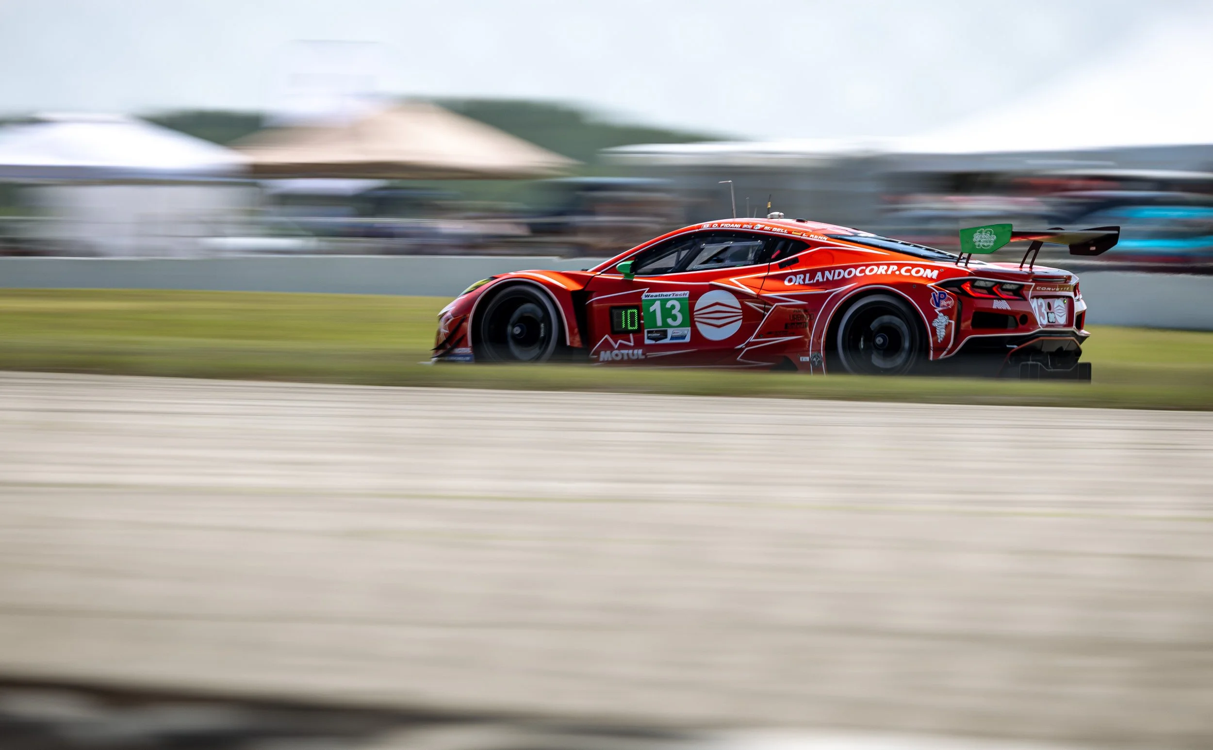 A red race car speeding on a race track with blurred background and motion blur effects.