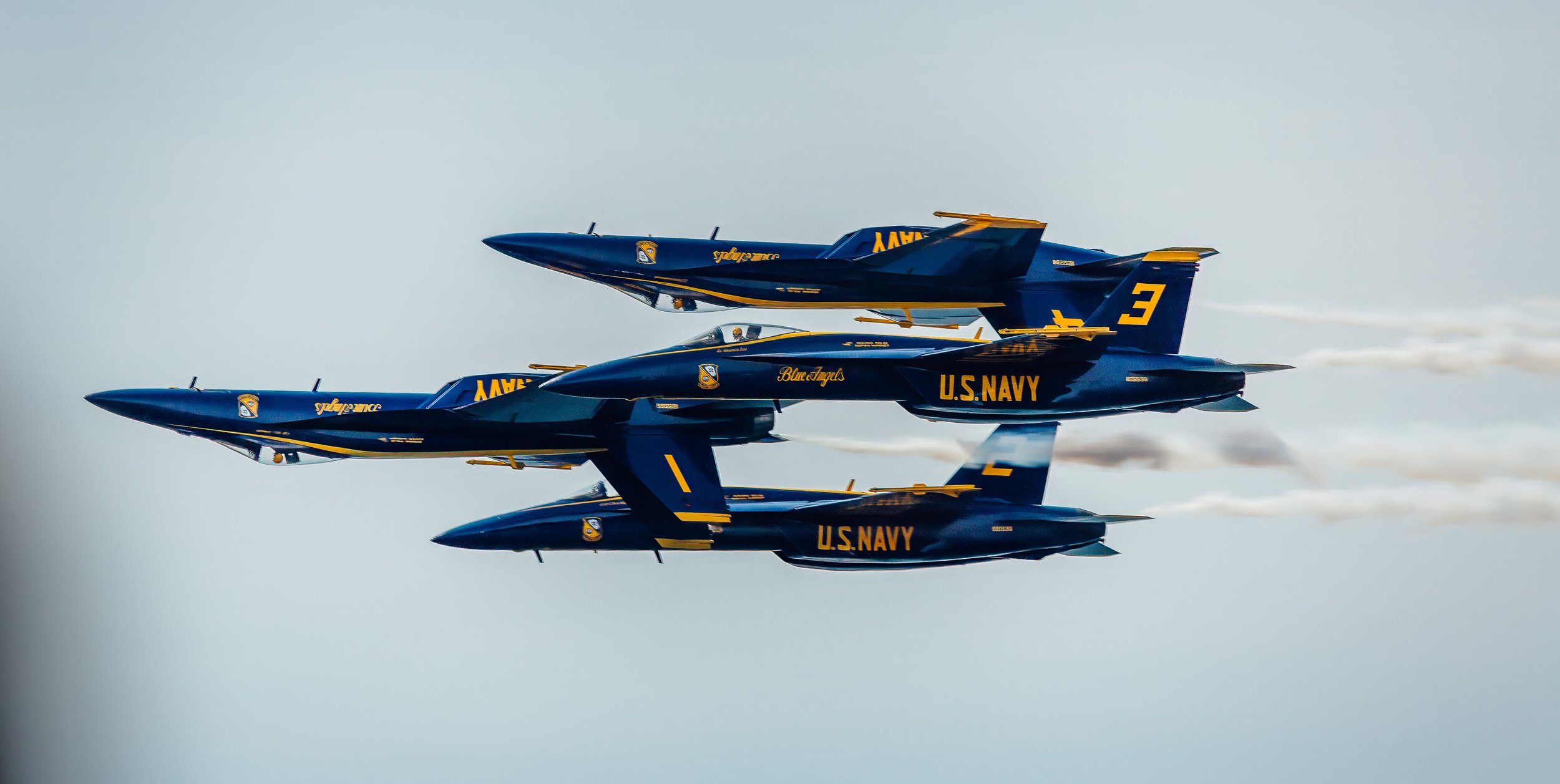 Three U.S. Navy blue fighter jets flying in formation against a cloudy sky.