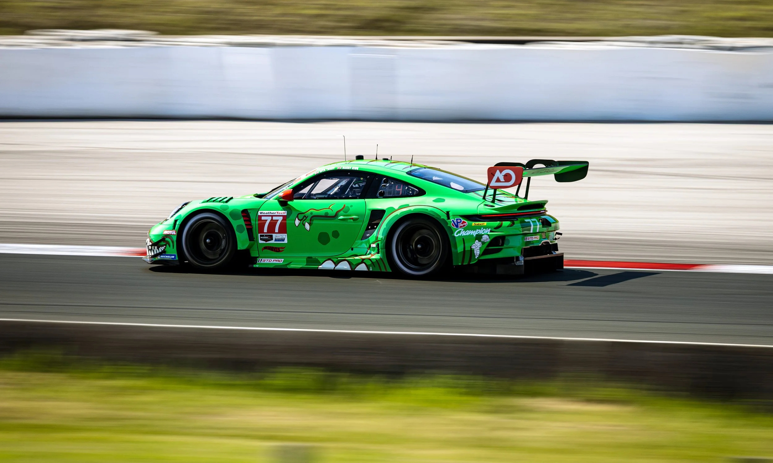 A bright green race car with a dragon design and the number 77 on it, speeding on a race track with a blurred background.