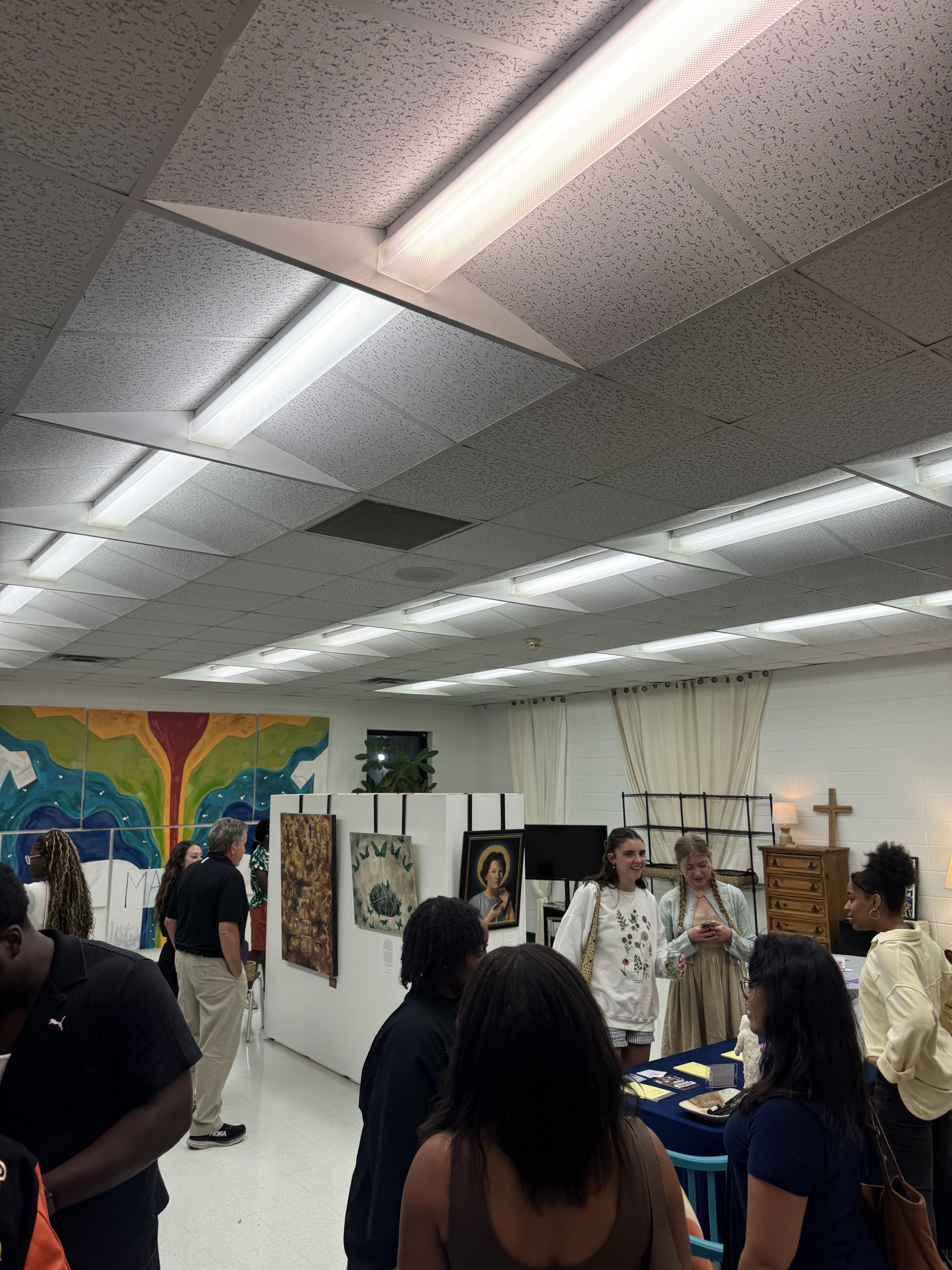People gathered in an indoor space with artwork and displays, some standing and some sitting, engaged in conversation.