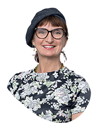 A smiling woman with short hair, glasses, wearing a floral top and a dark beret.