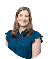 Portrait of a smiling young woman with long brown hair, wearing a blue polka dot top, against a white background.