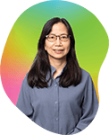 Portrait of a woman with long dark hair and glasses, wearing a blue top, standing against a colorful gradient background