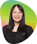 A woman with long dark hair wearing glasses and a black shirt, standing outdoors with a vibrant green and yellow background.