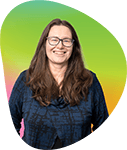 A woman with long, dark hair wearing glasses and a dark blue top, smiling in front of a colorful, gradient background.