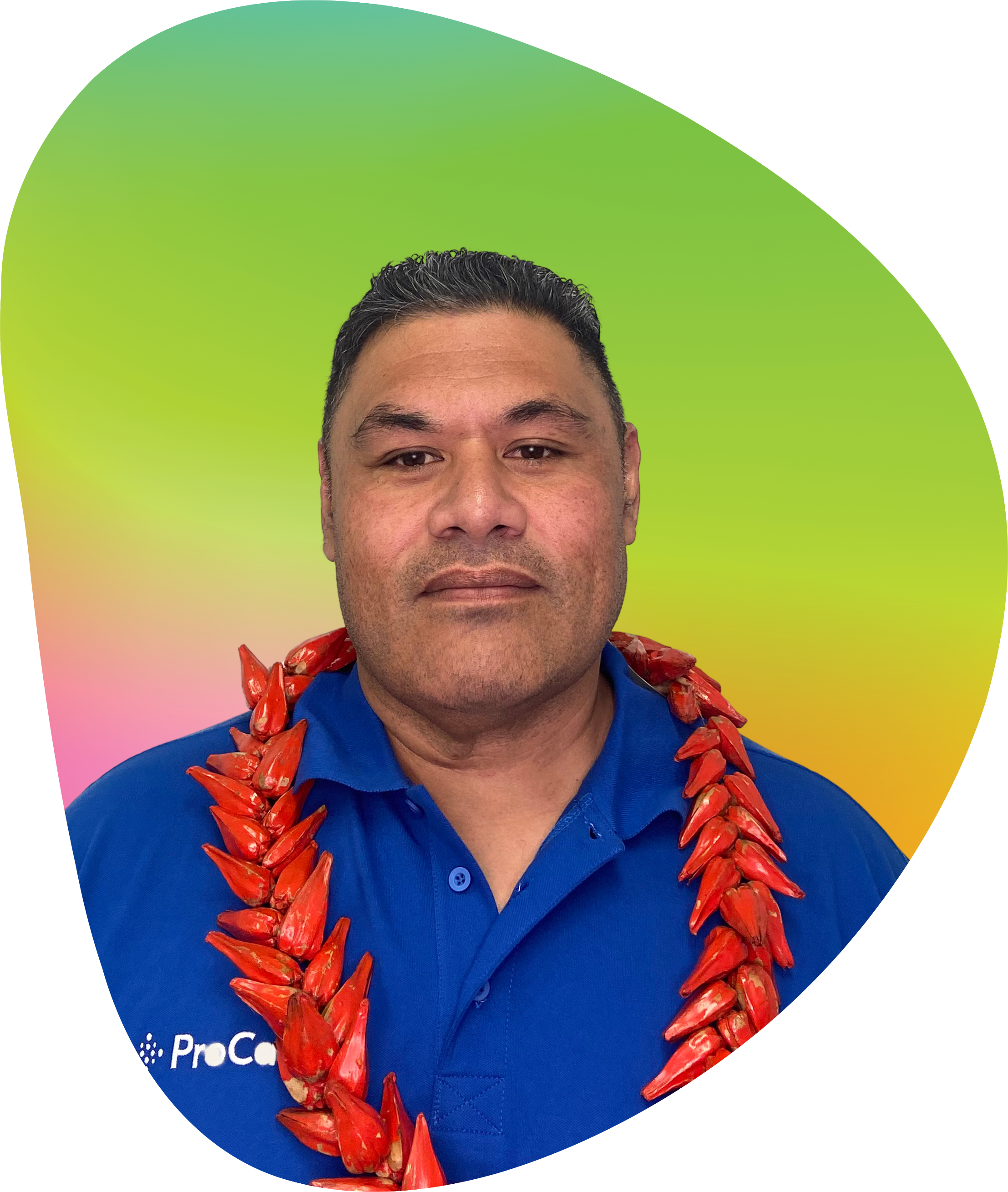A man wearing a blue shirt and a red floral lei around his neck, standing in front of a rainbow-colored background.