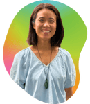 Smiling woman with shoulder-length hair wearing a light blue top and necklace, standing in front of a vibrant rainbow-colored background.