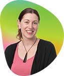 A woman with brown hair smiling, wearing a pink top and black jacket, standing in front of a gradient background.