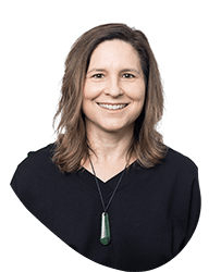 A woman with shoulder-length brown hair smiling, wearing a black top and a green pendant necklace, against a white background.