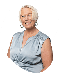 Portrait of an older woman with short white hair, wearing a light blue sleeveless top, smiling against a plain white background.