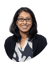 Portrait of a woman with glasses, shoulder-length dark hair, smiling, wearing a blazer and patterned blouse, against a white background.