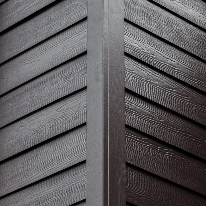 Close-up of dark brown wooden exterior siding with vertical trim at the junction.