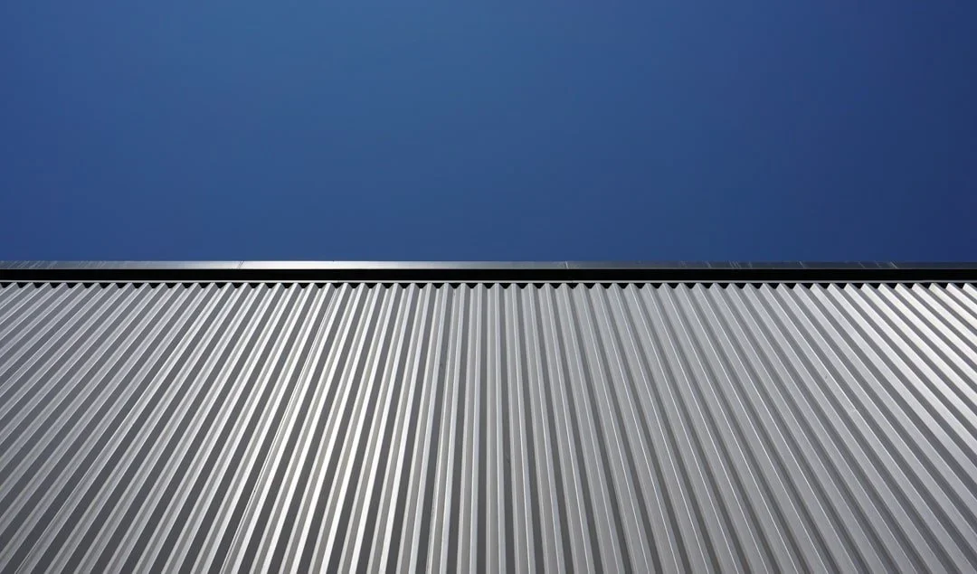 Close-up of gray corrugated metal siding with a blue sky background.