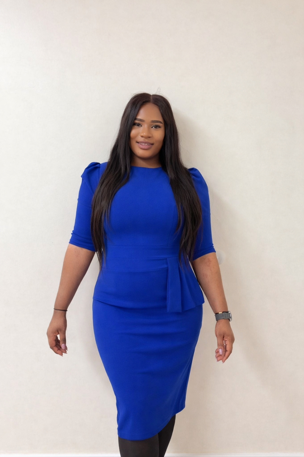 Woman in a royal blue dress standing in front of a plain white wall.