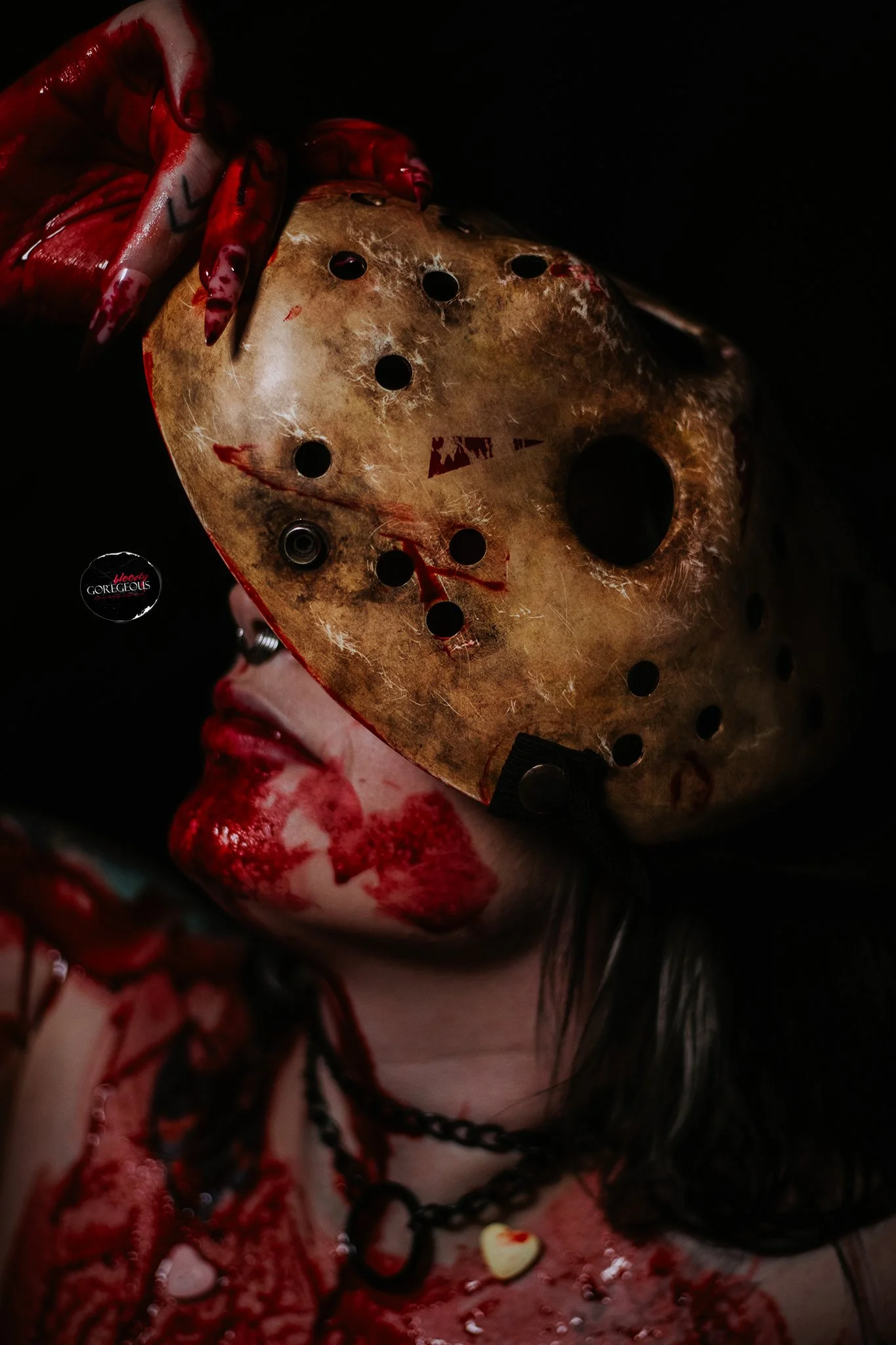 A person holding a bloody, weathered hockey mask with black eye holes, surrounded by blood and blood-stained jewelry.