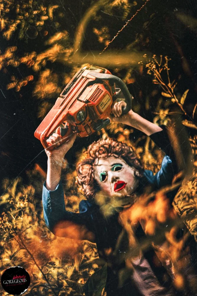A person wearing a creepy doll mask wielding a chainsaw amidst tall grass and trees at night.