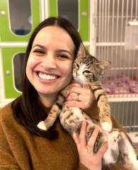 A woman smiling and holding a small tabby kitten in front of a green and white cage.