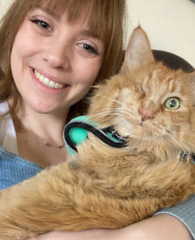 A woman smiling holds a fluffy orange cat with a collar.