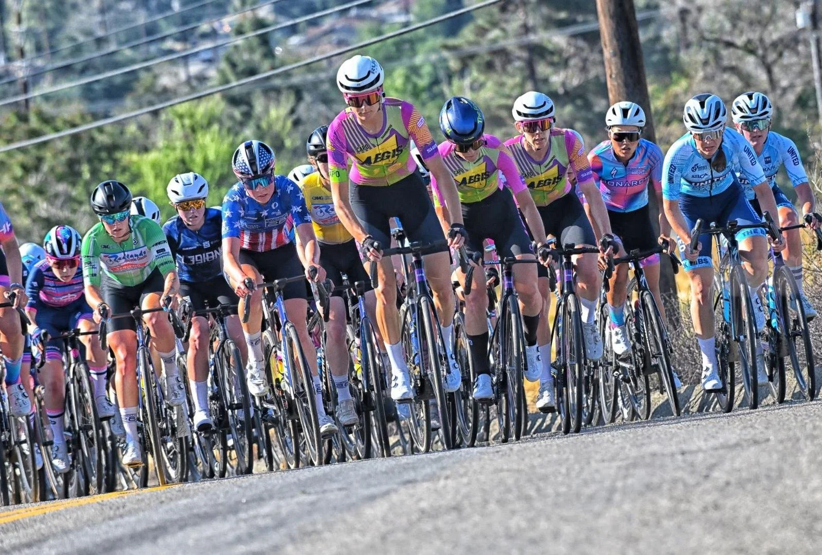 Group of female cyclists in colorful jerseys and helmets participating in a bicycle race on a rural road.