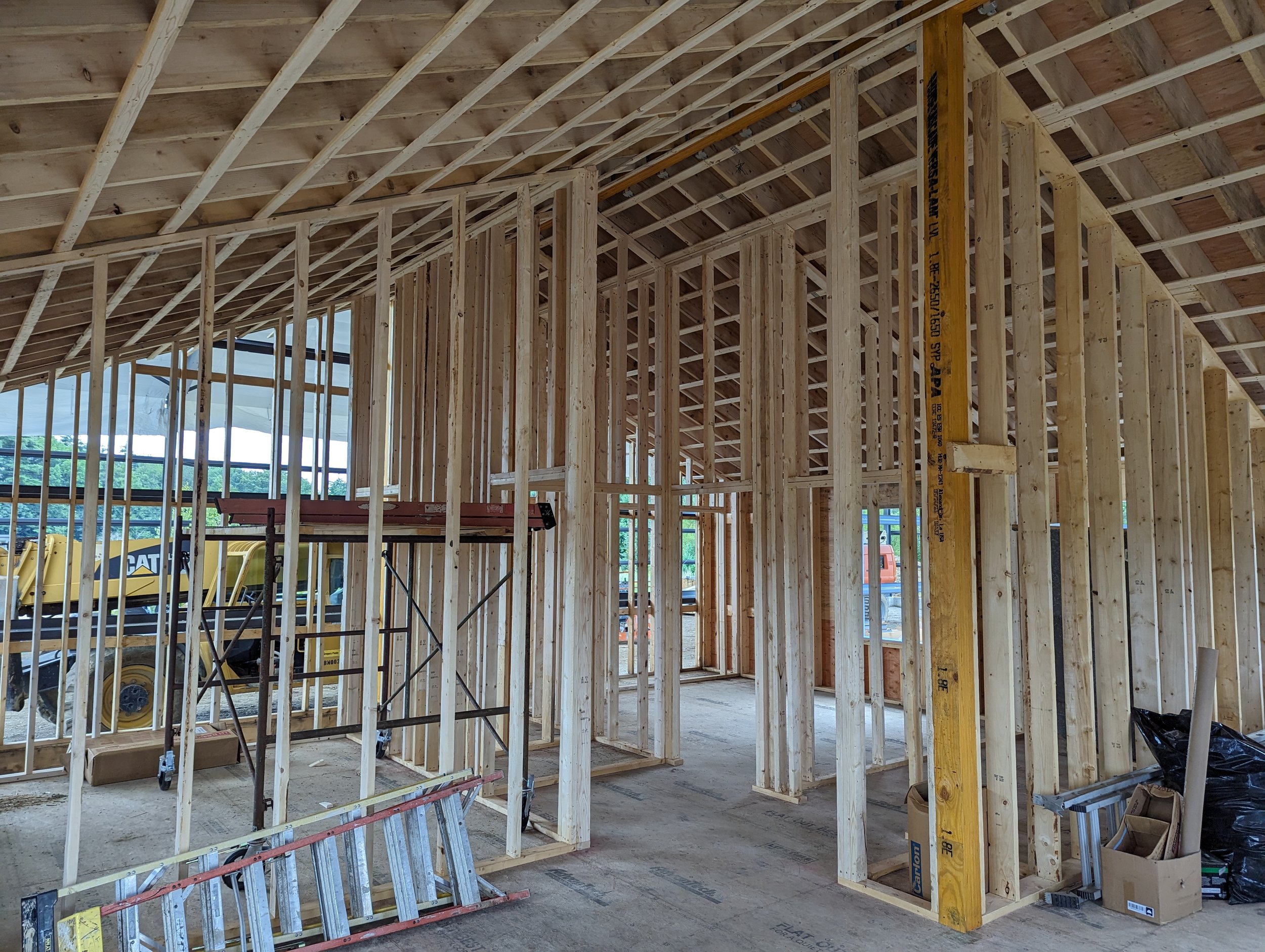 Interior view of a house under construction with exposed wooden framing, studs, and roof trusses.