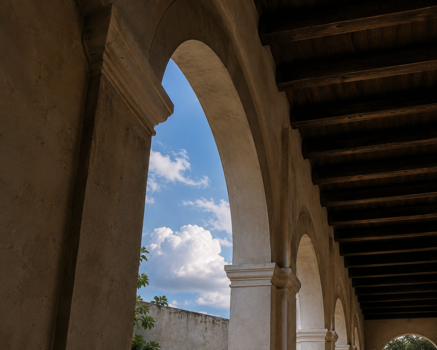 Stucco arcade with arched openings framing blue sky and white clouds.