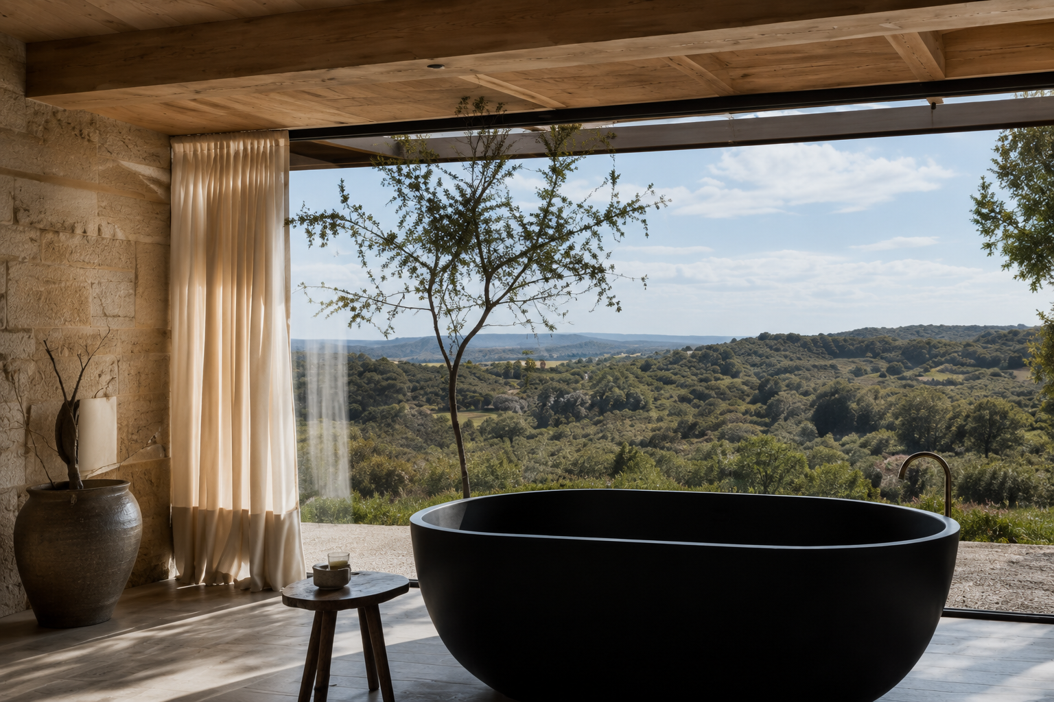 Black freestanding bathtub beside floor-to-ceiling windows overlooking the Hill Country landscape.