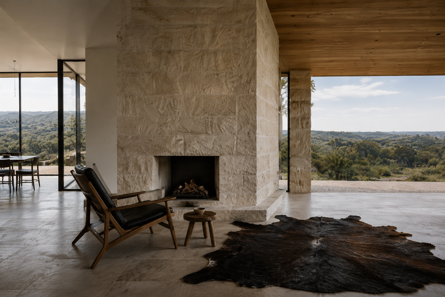 Limestone fireplace beside a leather chair and dark hide rug on a covered terrace overlooking the hills.