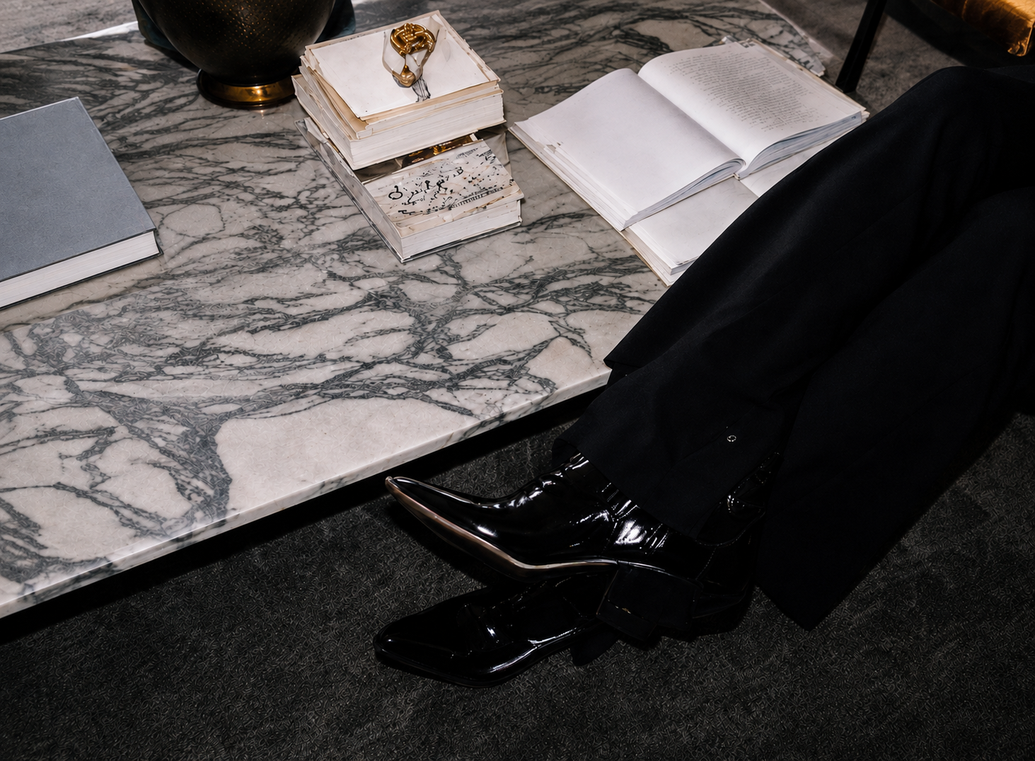 Veronica Lee Estes seated at a marble table with open books, wearing black patent leather boots.