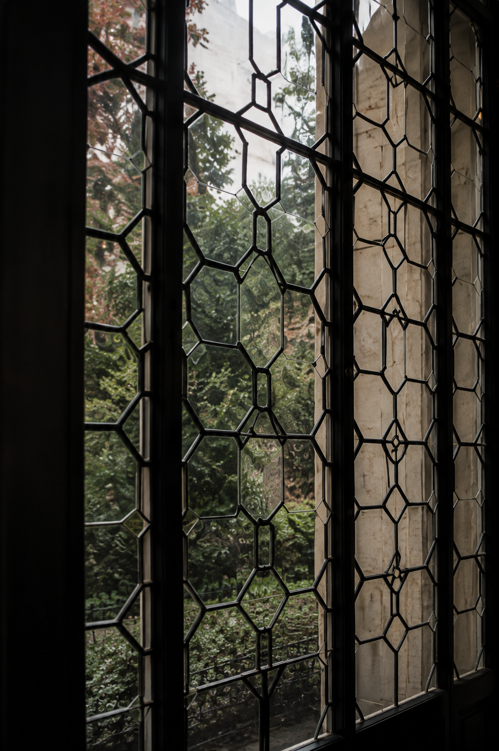Decorative leaded-glass window with geometric black framing and trees visible beyond.