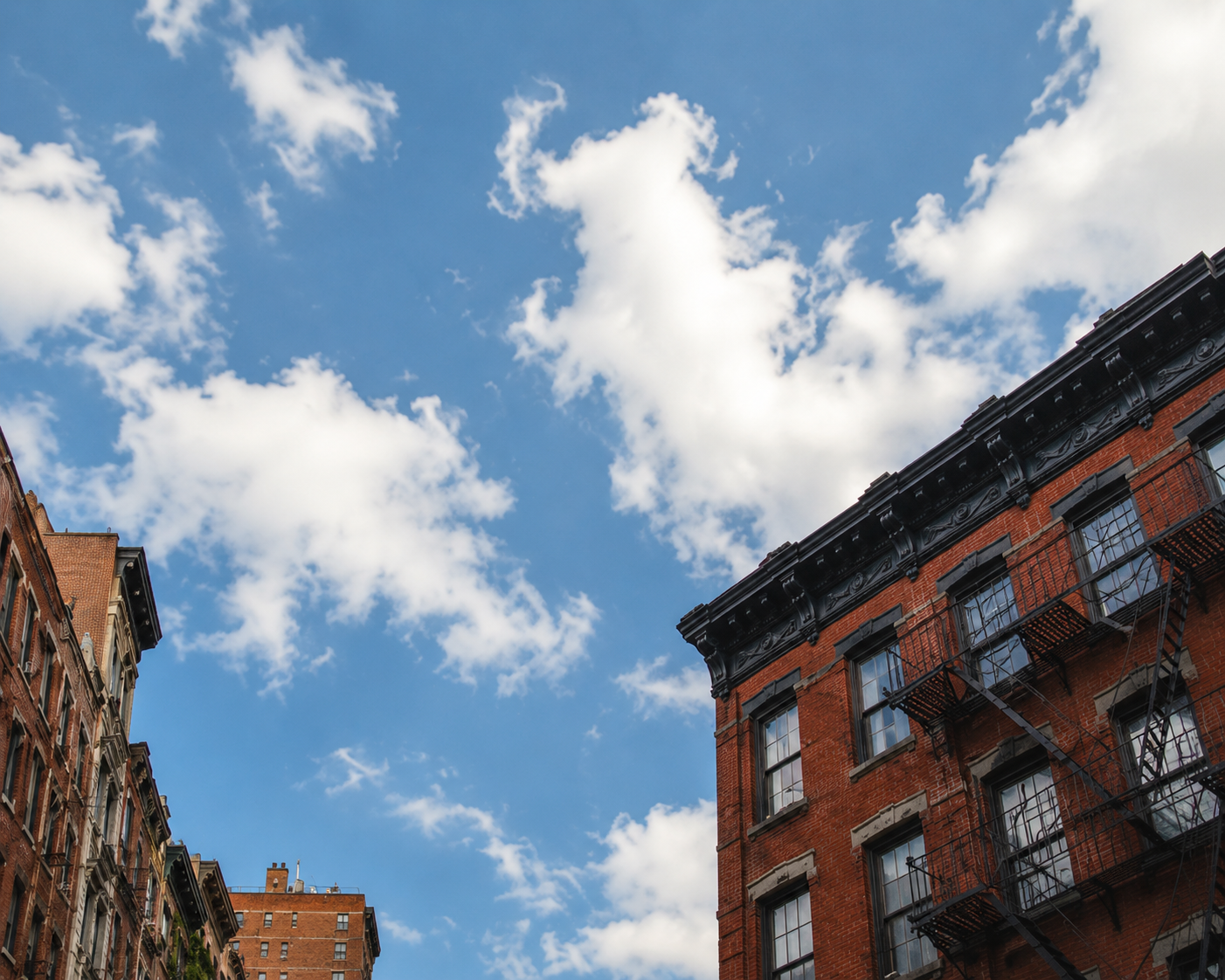 Blue sky and white clouds framed by the upper stories of a red brick building.