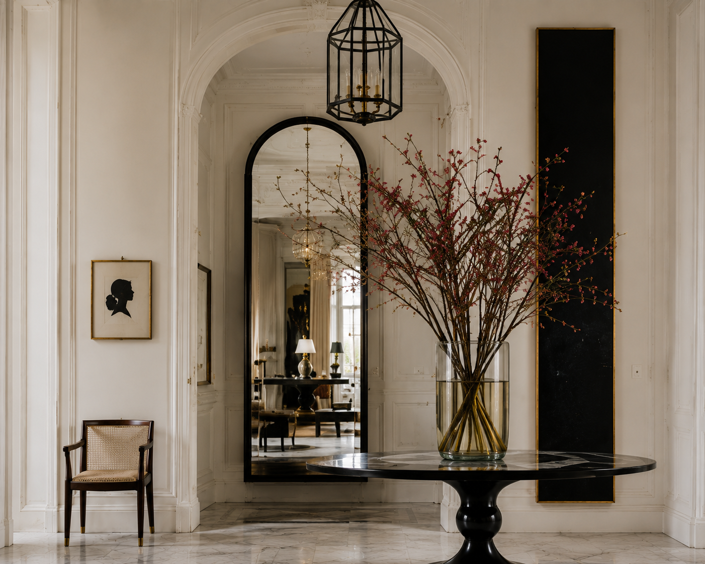 Arched interior passage with oversized mirror, flowering branches, marble floor, and black architectural details.