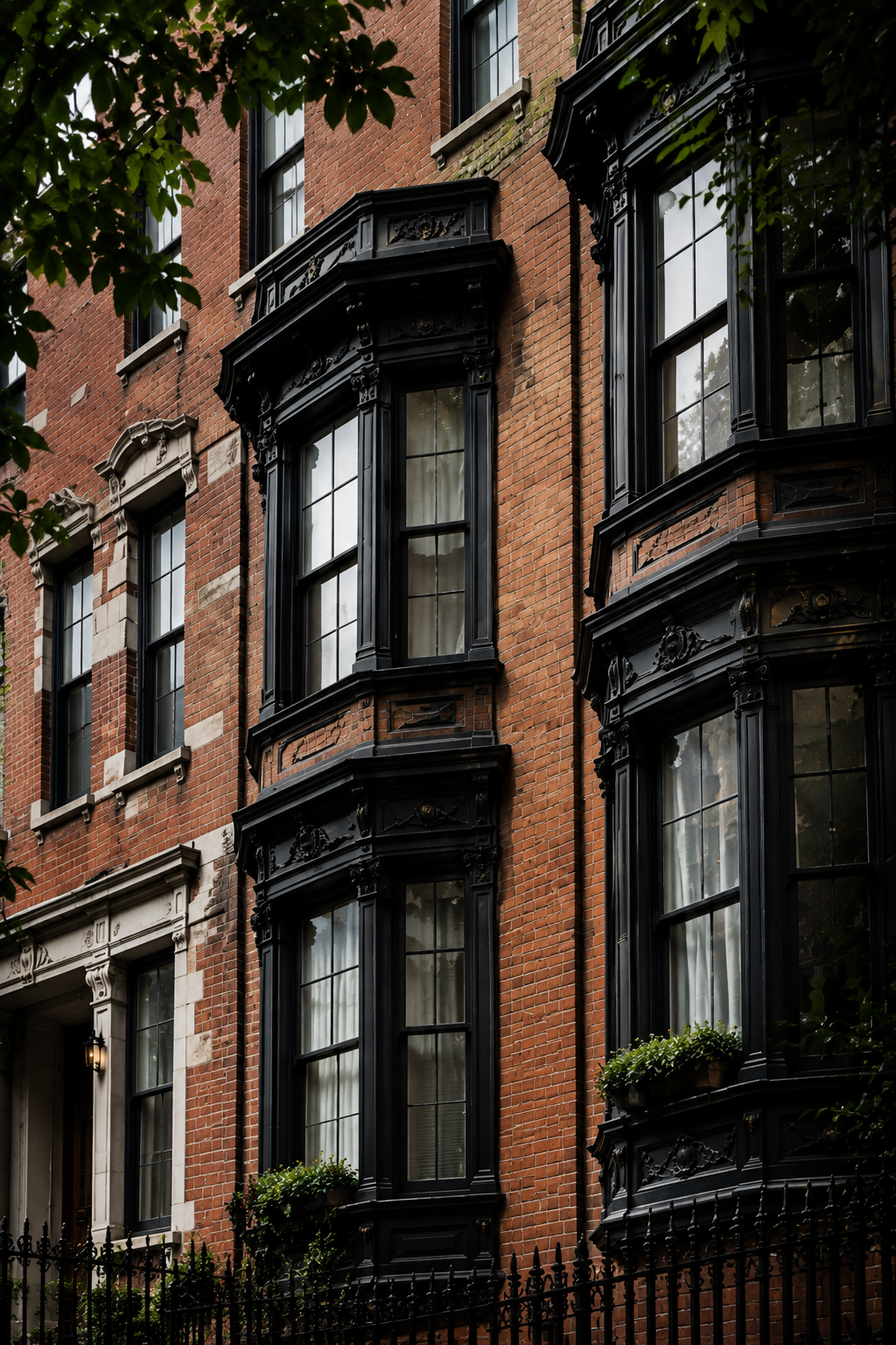 Red brick residential facade with projecting black bay windows and leafy branches.