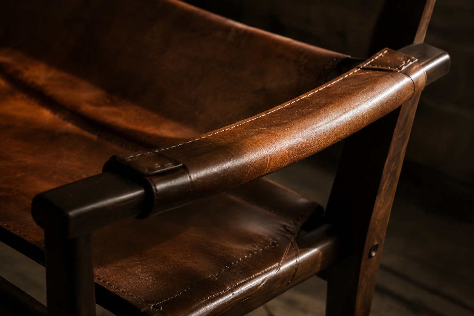 Close view of a weathered brown leather chair with stitched seams and wood frame.