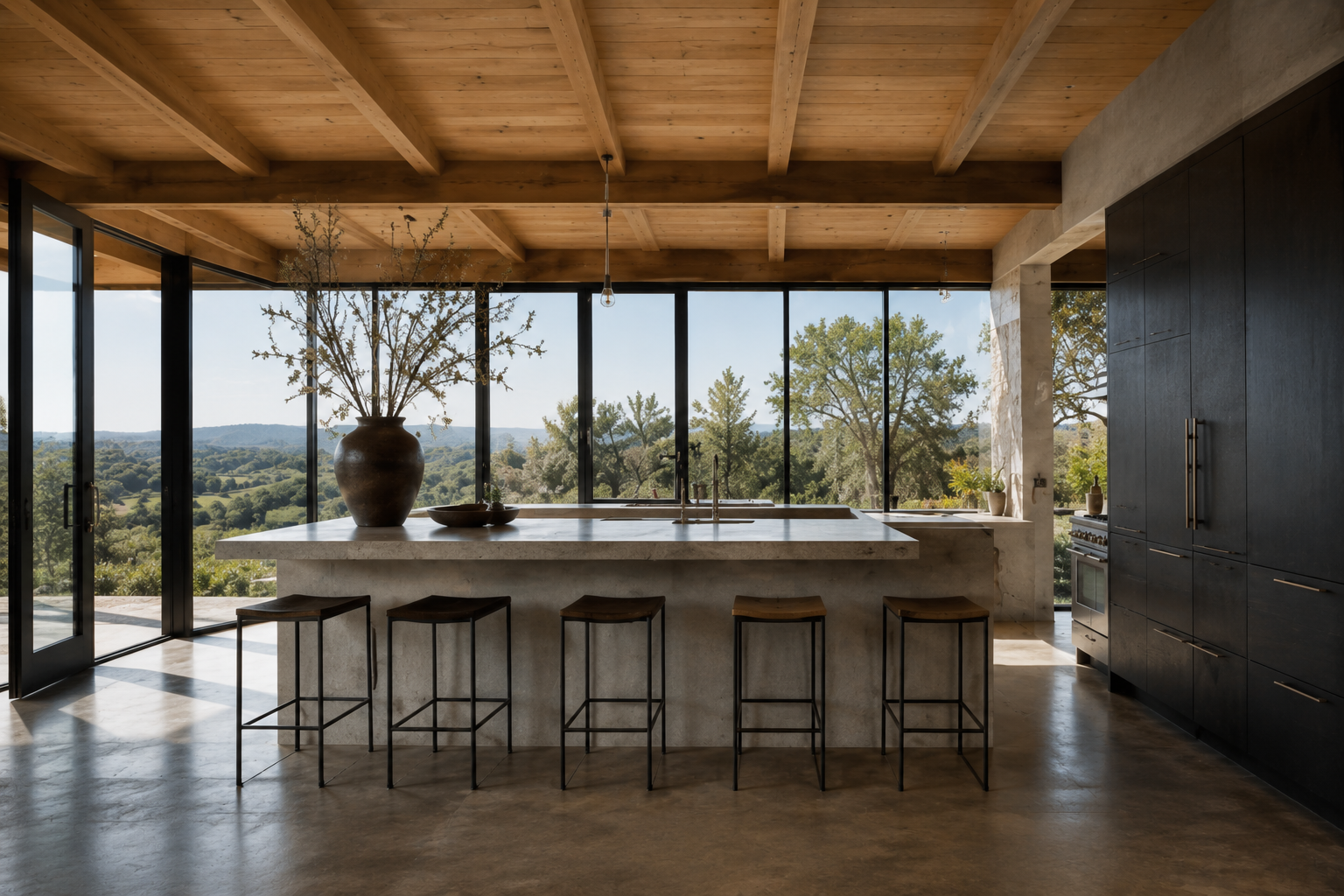 Open kitchen with a long stone island, counter stools, wood ceiling, and windows overlooking the landscape.