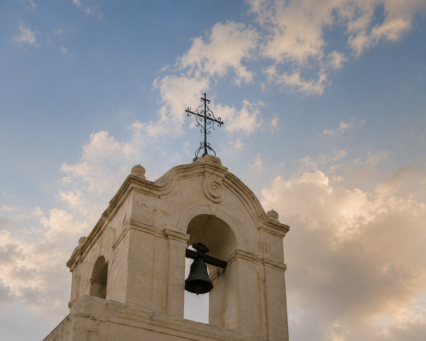 White stucco bell tower beneath a blue sky with scattered clouds.