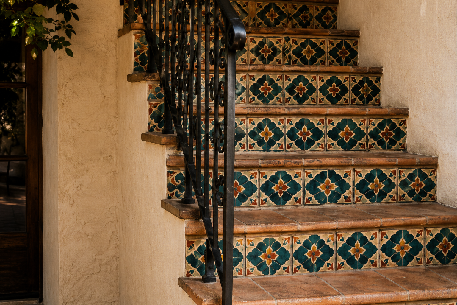 Decorative tiled staircase with wrought-iron railing against warm plaster walls.