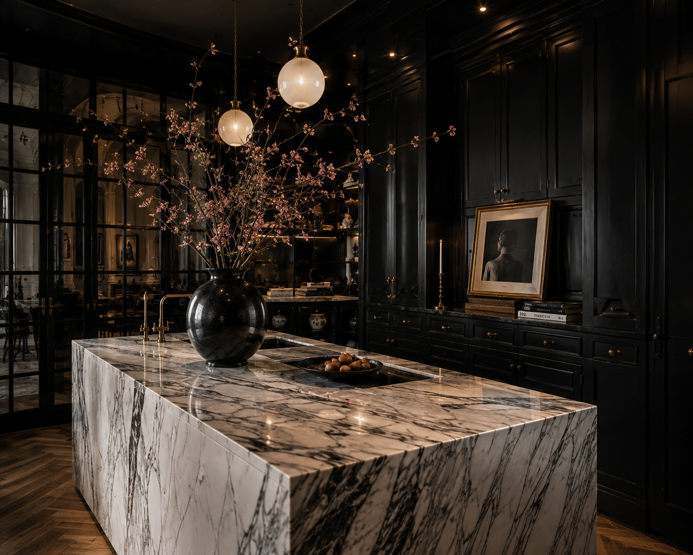 Dark kitchen with dramatic veined marble island, globe pendant lights, and flowering branches.