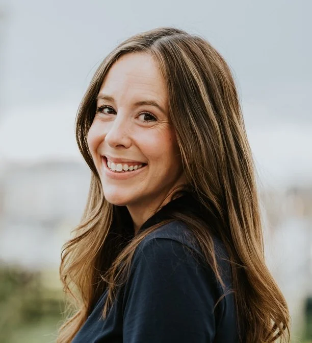 Smiling woman with long brown hair outdoors, wearing a dark top.