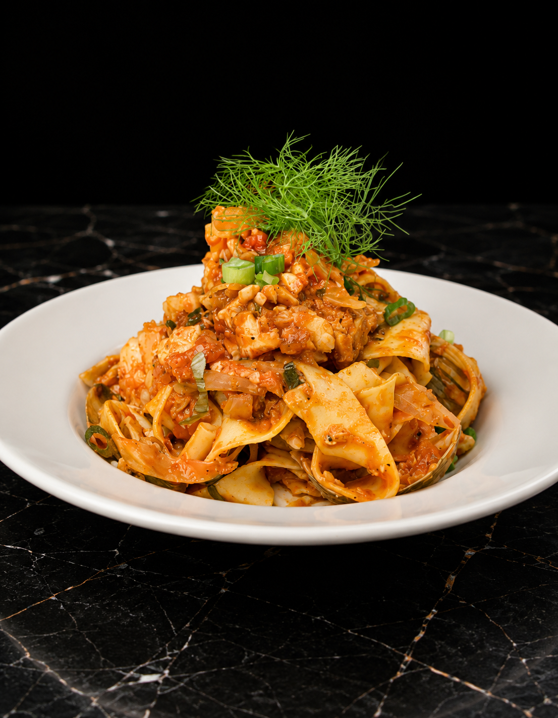 Plate of pasta with tomato sauce, garnished with chopped green onions and fresh herbs on black marble surface.